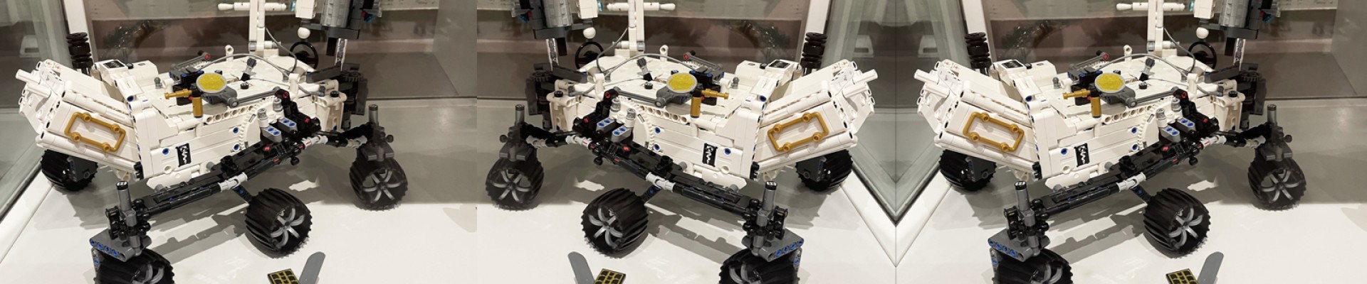 Ein LEGO-Modell eines Mars-Rovers und einer kleinen Drohne, ausgestellt in einer Museumsvitrine, mit einer Spiegelung auf einer Glasoberfläche.: 