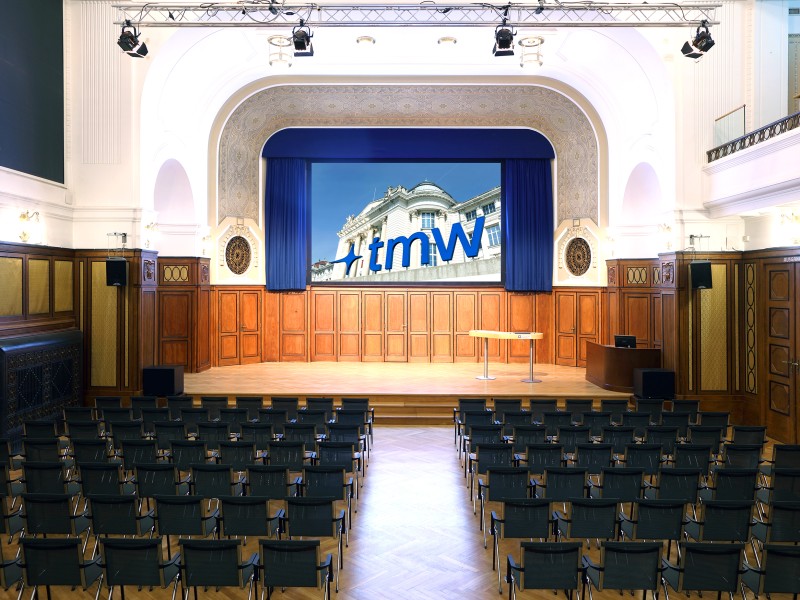Festsaal mit Bühne, Leinwand und Stuhlreihen im Technischen Museum Wien: