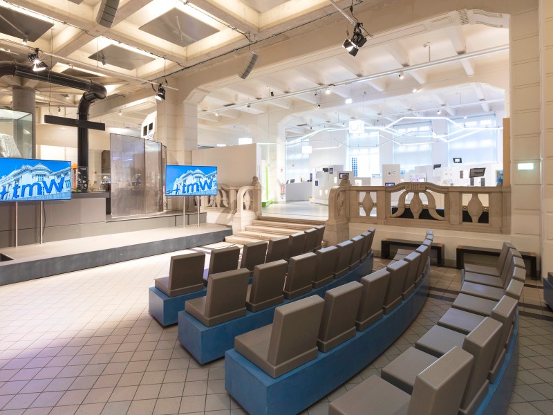 Vortragsbereich mit gebogener Sitzreihe und Bühne mit zwei Bildschirmen im Technischen Museum Wien: