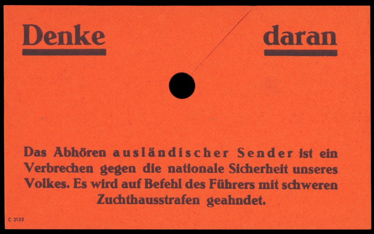 Ein rotes Hinweisschild, direkt an einem Radio angebracht, warnt vor den schwerwiegenden Folgen des Hörens ausländischer Sender. Dieses Schild stammt aus der Zeit des Nationalsozialismus und verdeutlicht die Zensurmaßnahmen des Regimes: Hinweisschild „Denke daran“