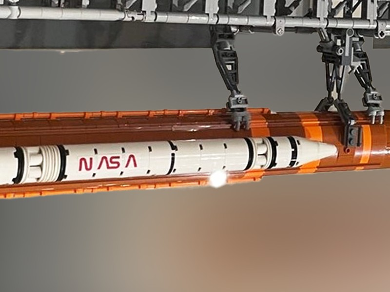 Ein detailliertes Modell einer NASA-Rakete mit orangefarbenen und weißen Abschnitten, ausgestellt in einer Startvorbereitung mit strukturellen Halterungen.: 