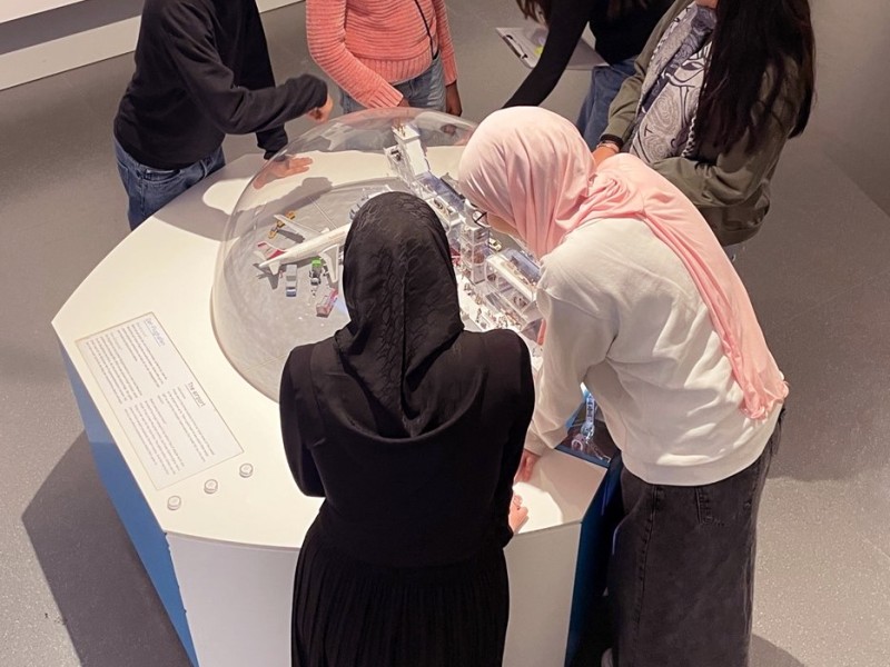 A group of people gathered around a circular exhibit in a museum, interacting with a model under a transparent dome.: Visit to the exhibition <i>In Motion</i>. Inspired by current hands-on objects, MISSION CONTROL has developed ideas for a future exhibition.