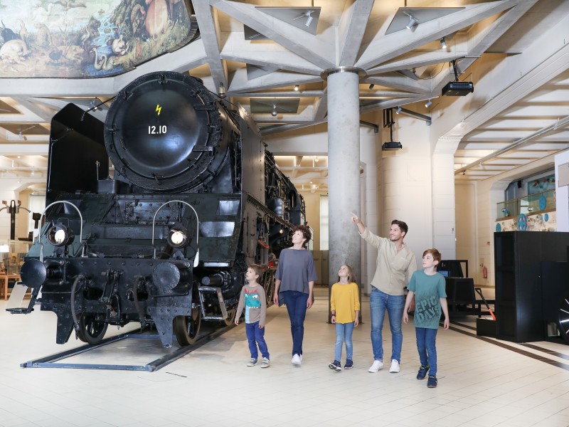 Eine Familie sieht sich gemeinsam die 12.10er Dampflokomotive an. In der Ausstellung "12.10 eine Dampflokomotive der Superlative" : 